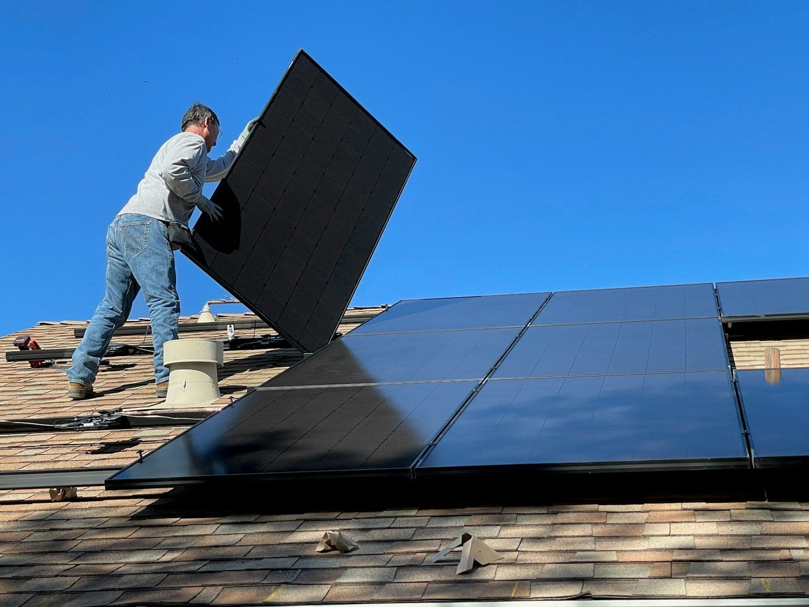 An installer fitting a solar panel on a roof under a clear sky